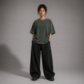 Person wearing a loose-fitting green t-shirt and black pants against a gray background