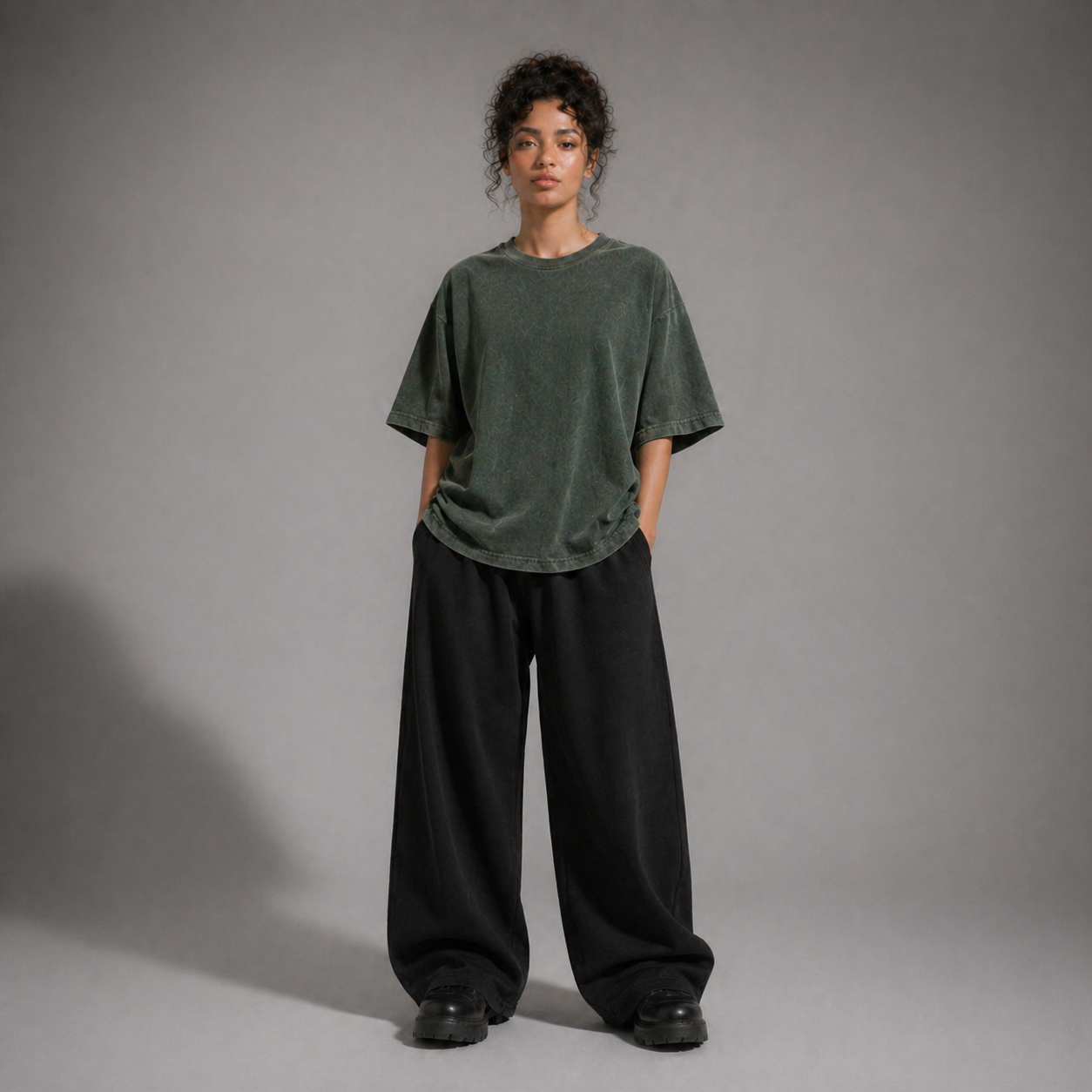 Person wearing a loose-fitting green t-shirt and black pants against a gray background
