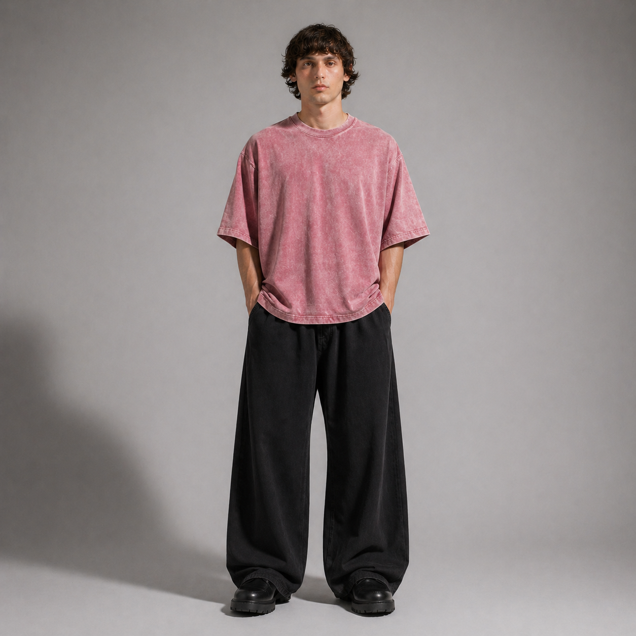Person wearing a pink t-shirt and black pants against a gray background