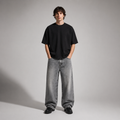 Person wearing a black t-shirt and gray jeans standing against a plain background