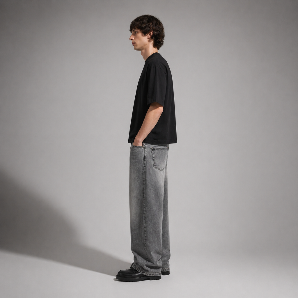 Person wearing a black t-shirt and gray jeans standing against a plain background