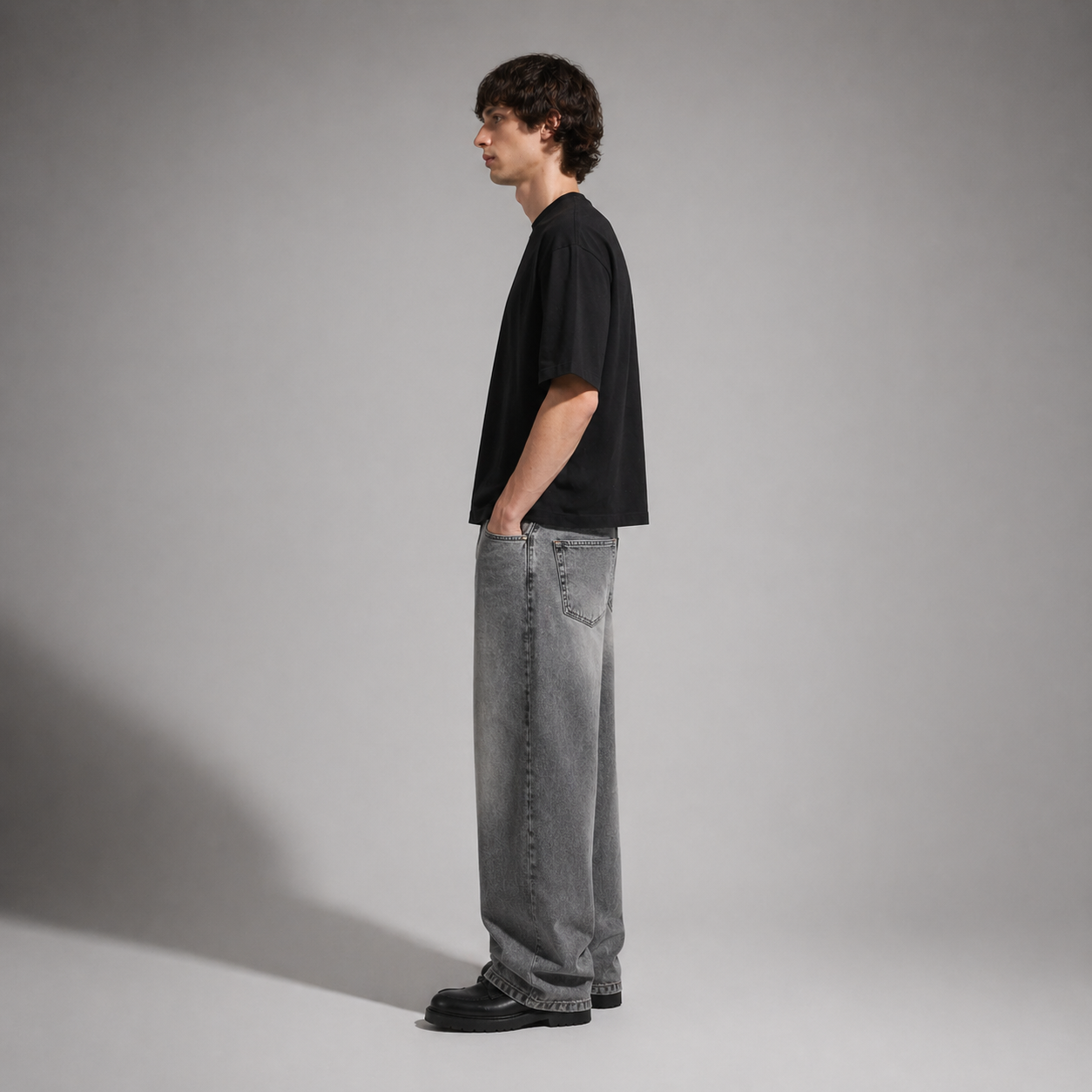 Person wearing a black t-shirt and gray jeans standing against a plain background