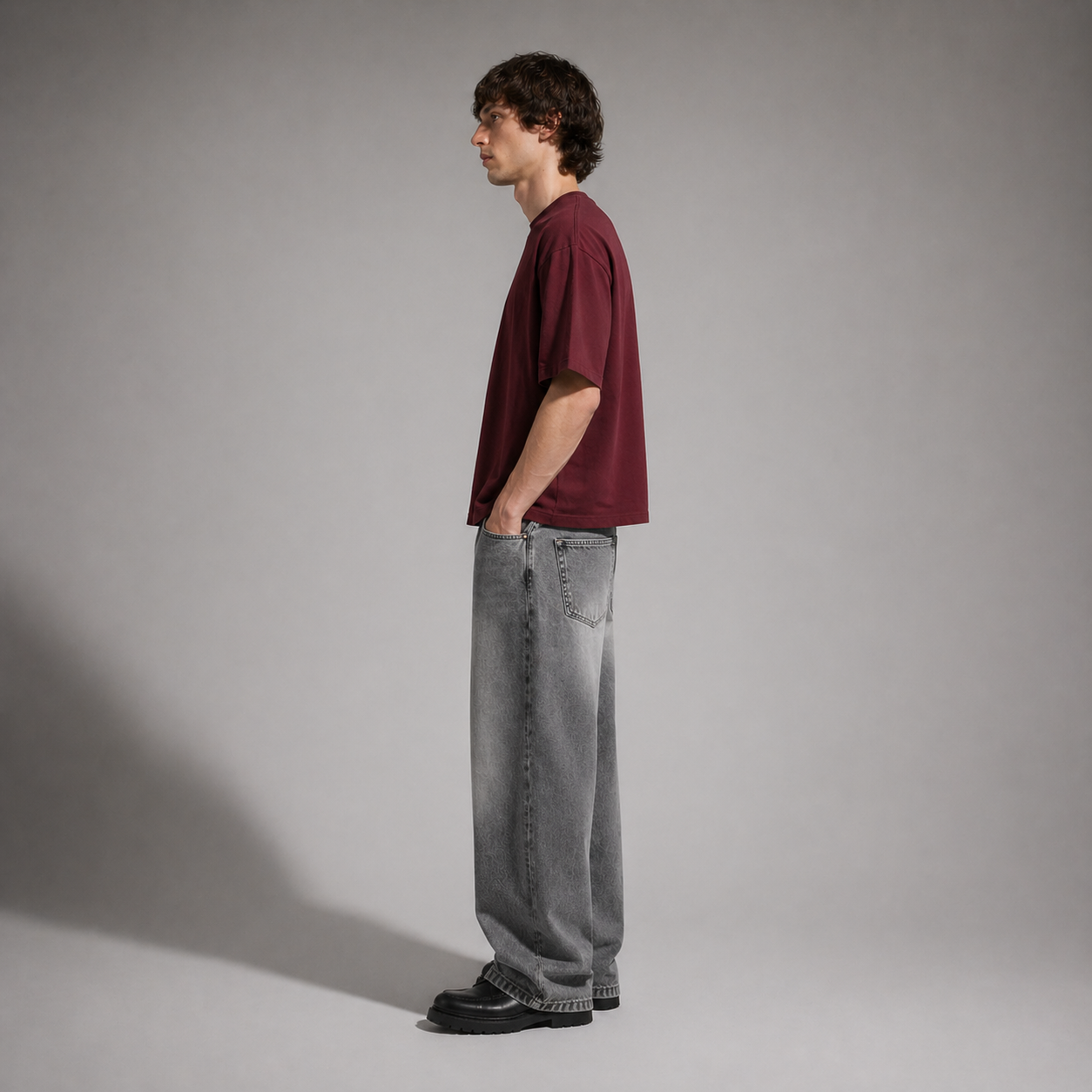 Person wearing a burgundy shirt and gray jeans standing against a plain background