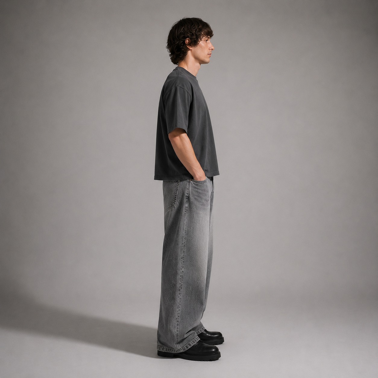Person wearing a dark gray t-shirt and light gray jeans standing against a plain background