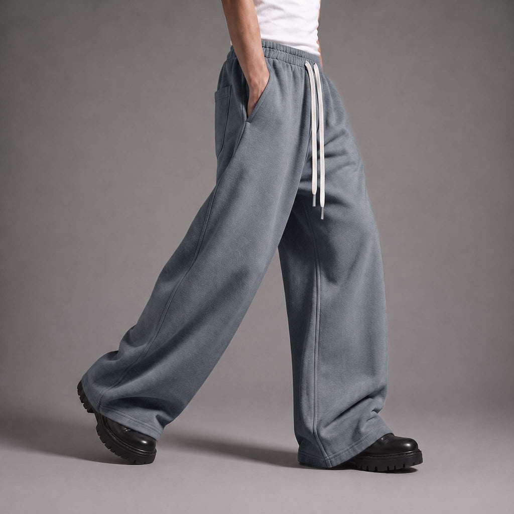 A person wearing wide-leg, relaxed-fit sweatpants in a dusty slate blue color with a white drawstring, paired with black platform shoes against a neutral gray studio background.