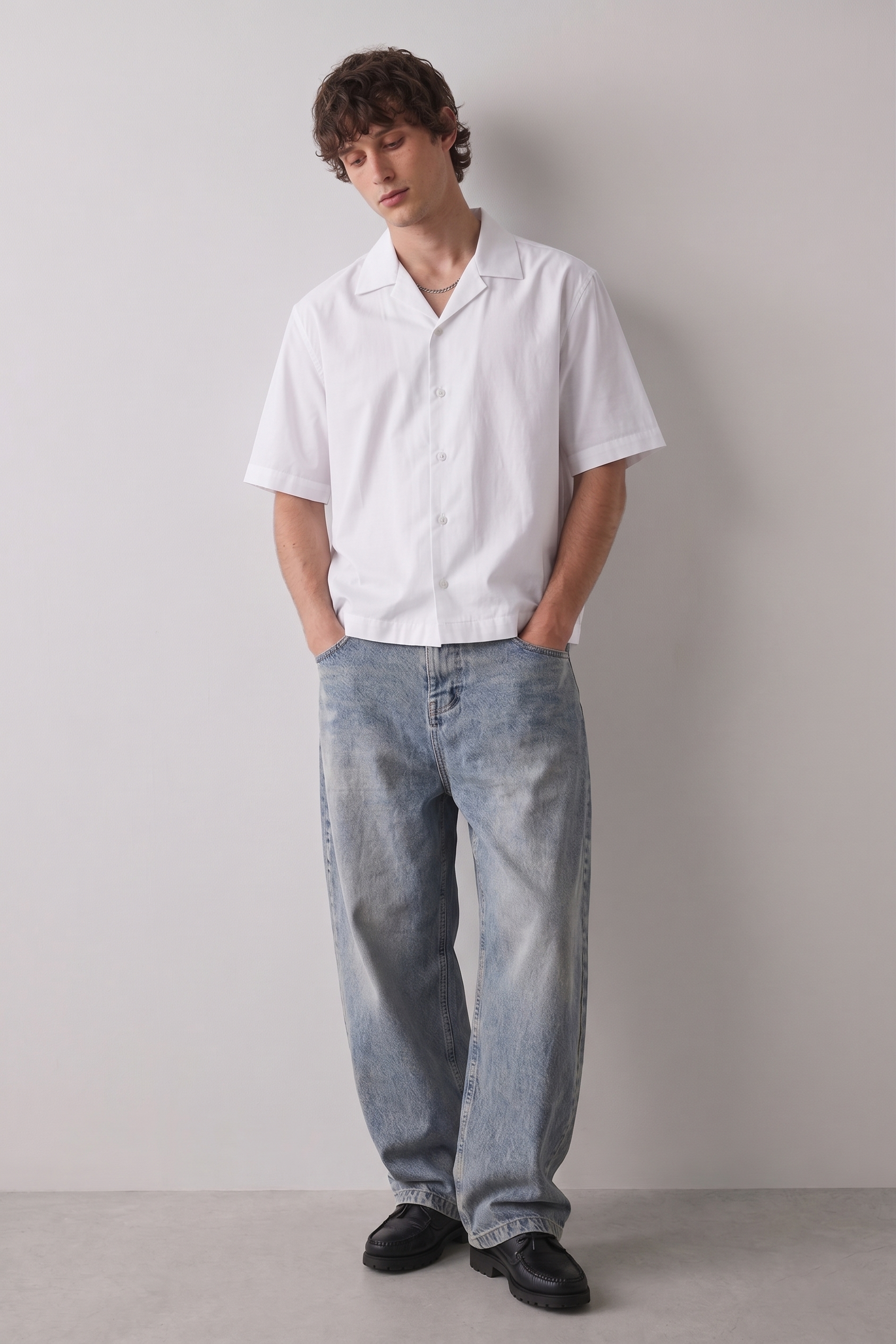 Person wearing a white shirt and light blue jeans against a plain background
